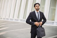 商务专业人士穿着西装夹克，扣着纽扣，在现代建筑外拿着公文包