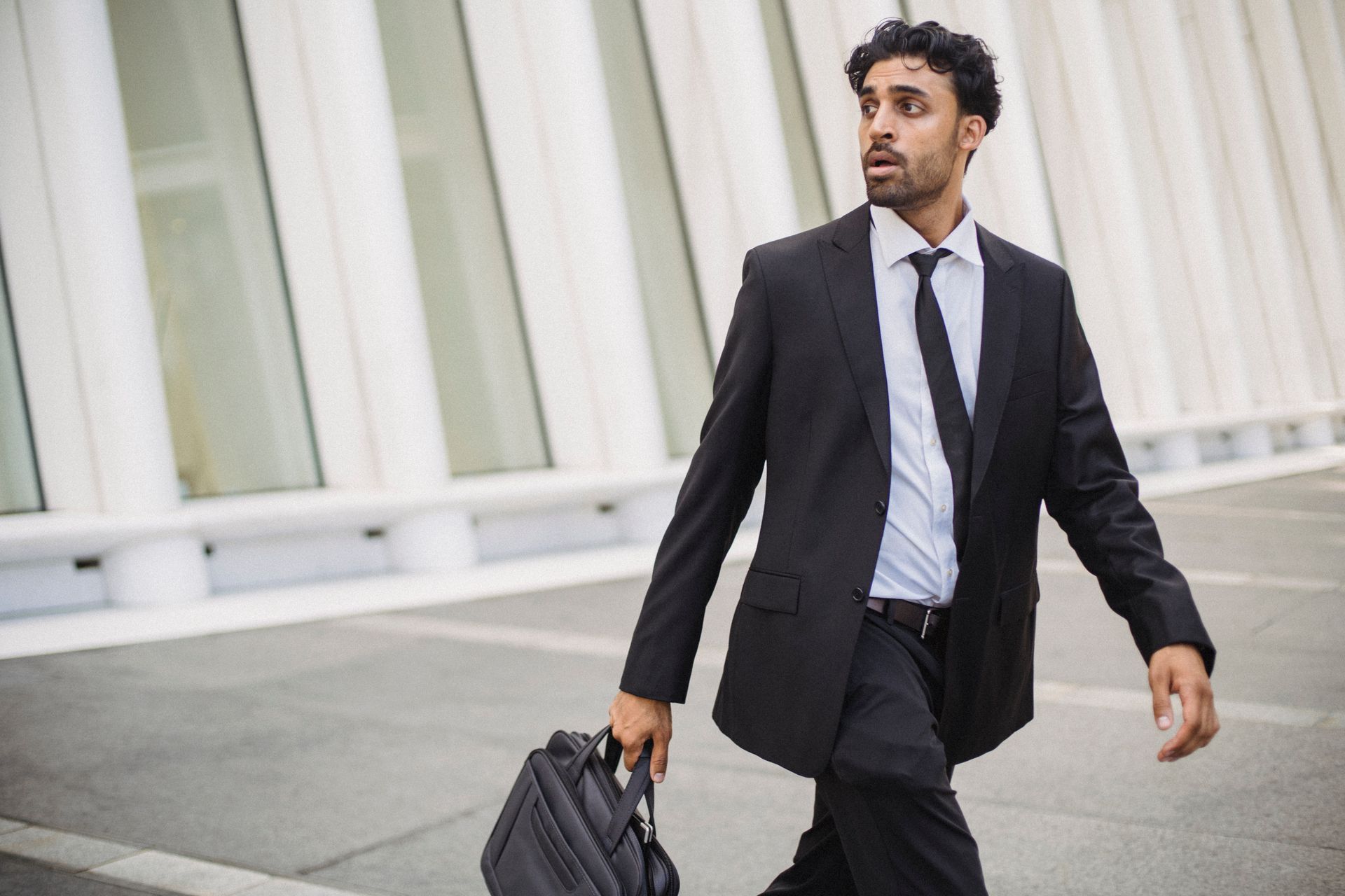 Confident businessman in corporate attire walking outside with a briefcase.
