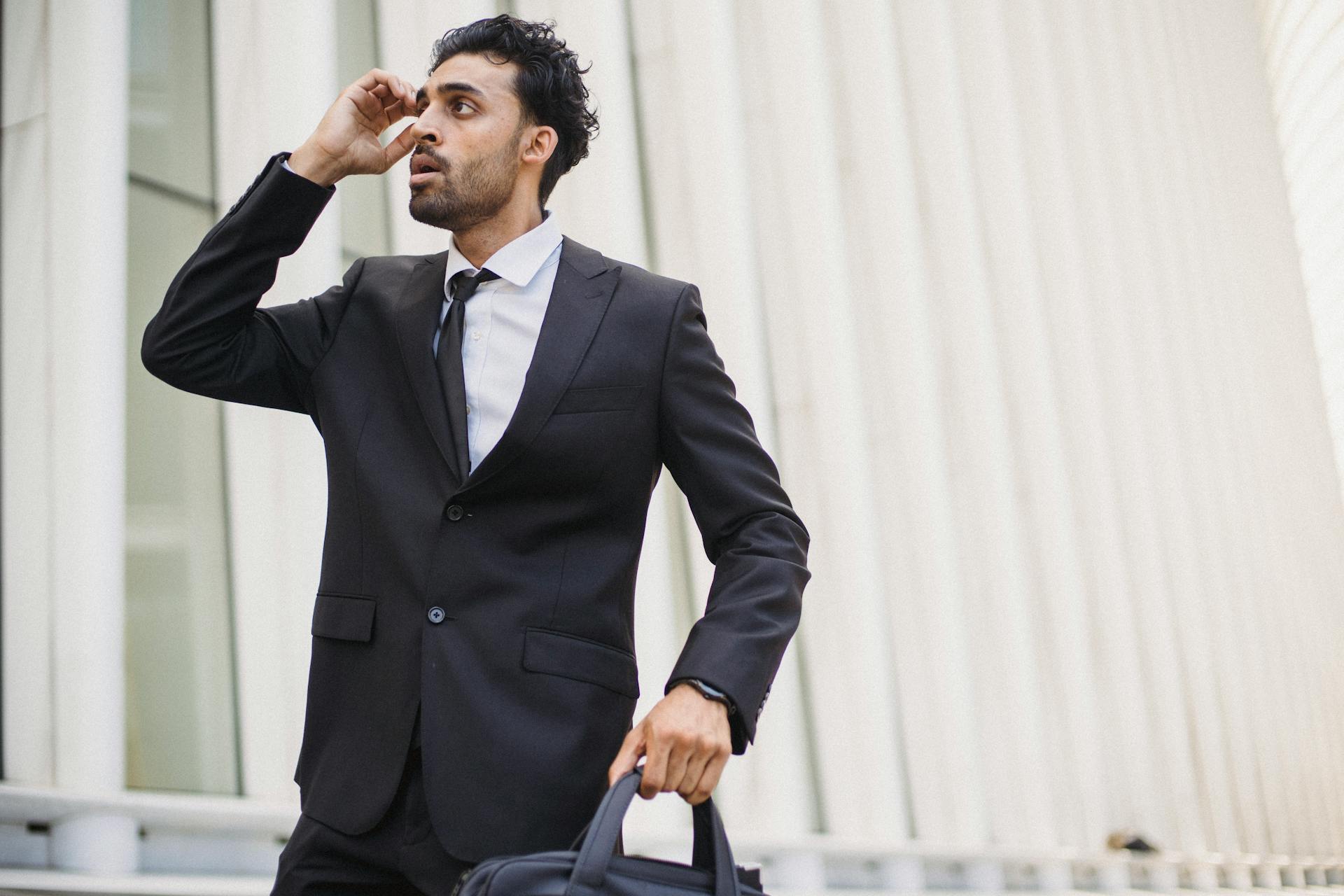 A young businessman in a suit, holding a briefcase and talking on the phone outside an office building.