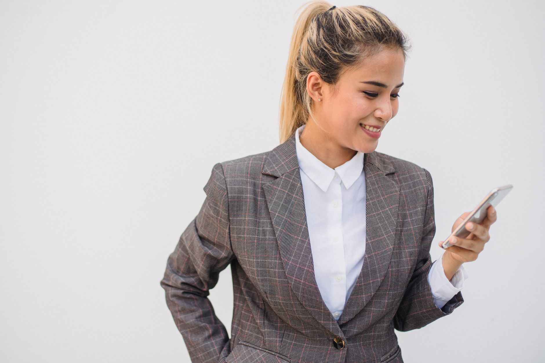 Happy young woman in plaid blazer texting on smartphone against a white background.