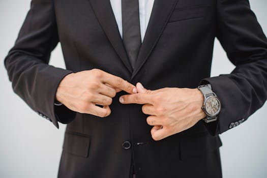 Close-up of a man's hands adjusting a black suit jacket, showcasing confidence and style.