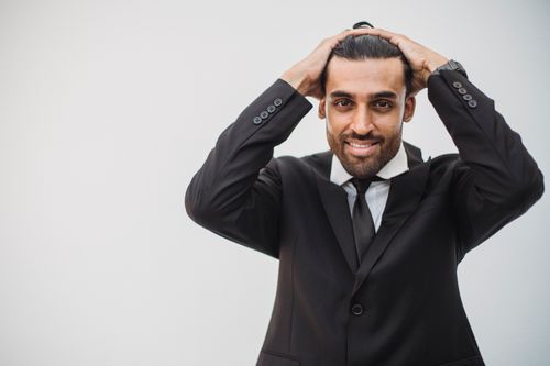 Free Smiling businessman in a black suit posing with hands on head on a white background. Stock Photo