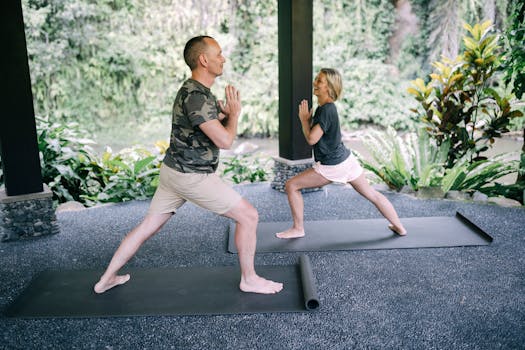 Couple practicing yoga outdoors on mats surrounded by lush greenery.
