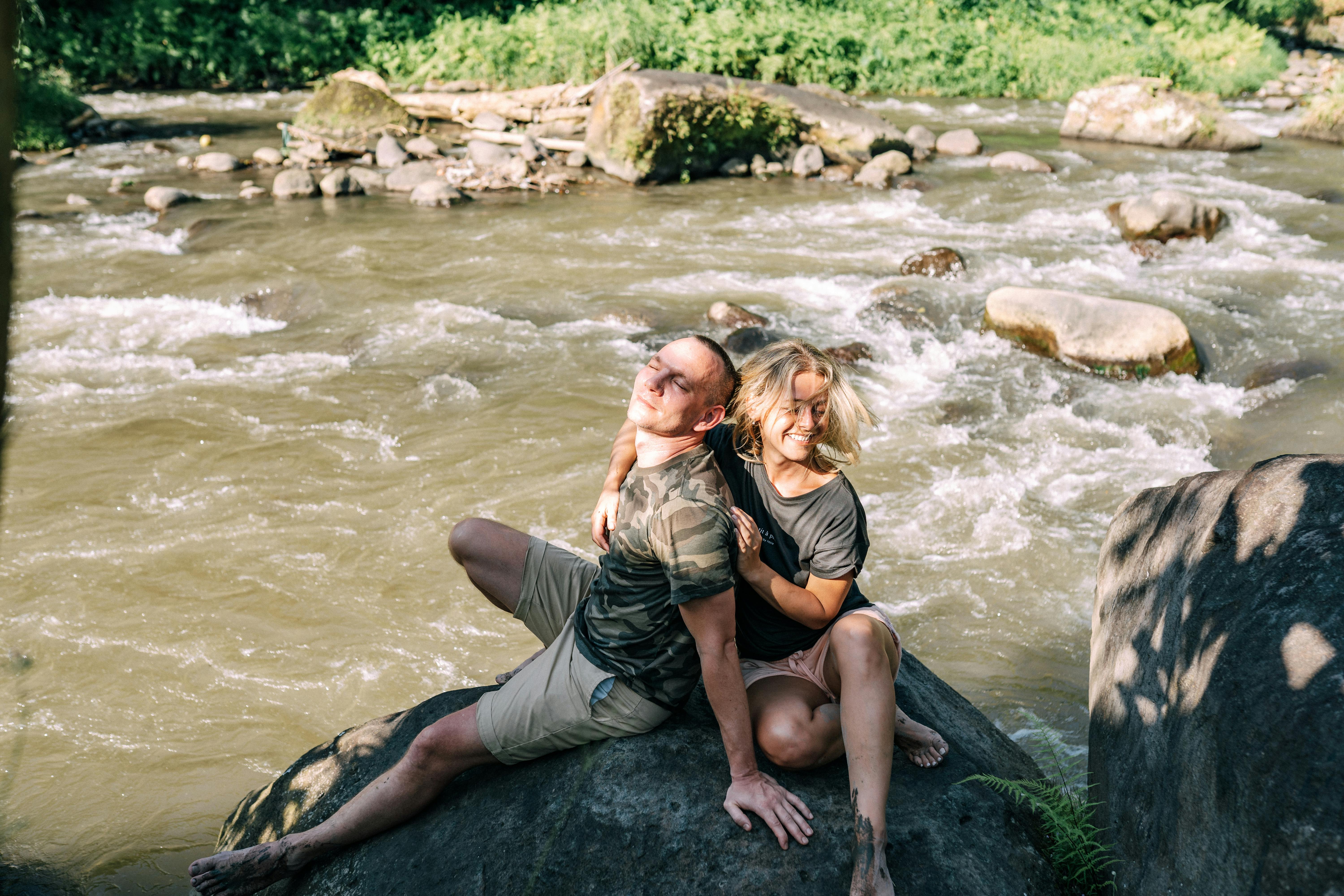 一对快乐的夫妇坐在河岸边的岩石上，微笑着享受阳光明媚的一天