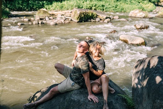 一对快乐的夫妇坐在河岸边的岩石上，微笑着享受阳光明媚的一天
