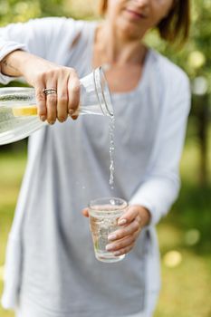 阳光明媚的日子里，一个女人将新鲜的柠檬水倒入玻璃杯中，象征着提神和健康