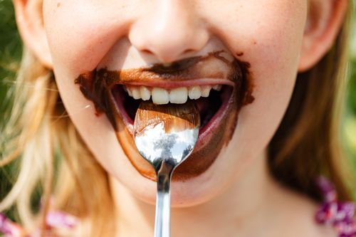 Free Close-up of a child's face enjoying a messy chocolate treat, smiling with a spoon. Stock Photo