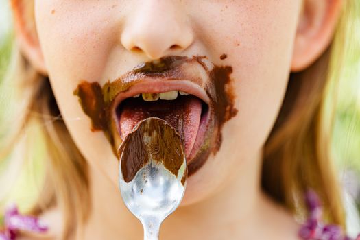 Close-up of a child eating chocolate with a spoon, messy and joyful.