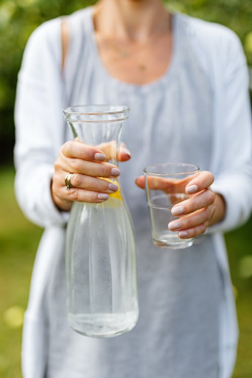 Wanita Berkemeja Lengan Panjang Putih Memegang Botol Kaca Bening Dengan Air