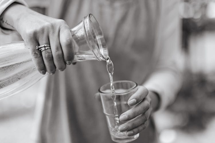 A Person Pouring Water On Clear Drinking Glass