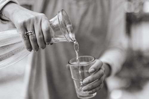 Free A close-up view of a woman pouring water from a carafe into a glass, highlighting hands and jewelry. Stock Photo