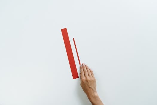 A minimalist composition featuring red paper strips and a human hand on a white background.