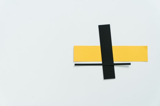 A minimalist composition featuring intersecting black and yellow paper strips on a white background.