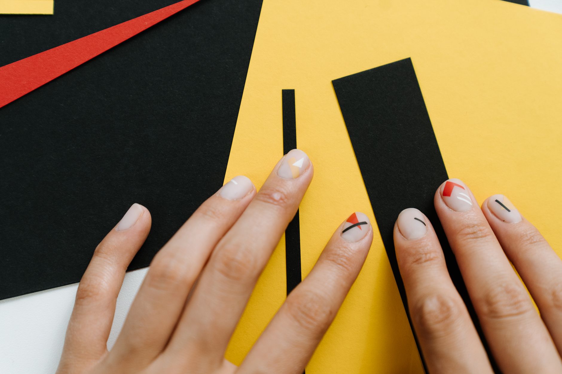 Close-up of modern nail art with geometric shapes on a yellow and black paper collage.
