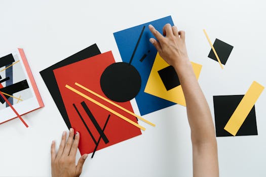 Hands arranging colorful geometric paper shapes in an abstract modern art style.