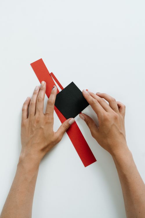 Free Hands arranging red and black paper shapes on a white surface. Stock Photo