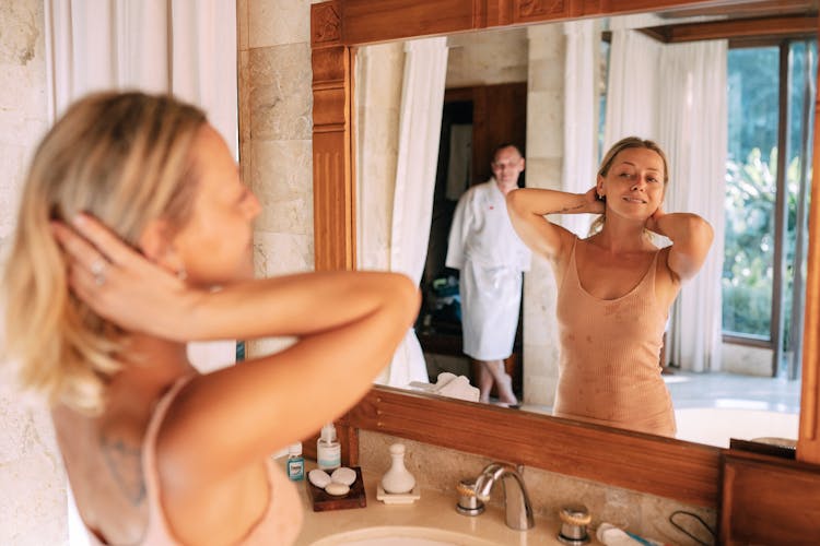 Woman Fixing Hair In Bathroom Mirror