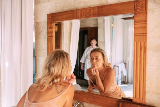 A woman applies makeup in a sunlit bathroom with warm, natural tones.