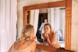 Woman Looking in Mirror in Bathroom Doing Makeup