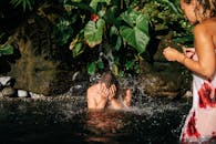 一个男人在热带游泳池中享受飞溅的清凉，四周环绕着郁郁葱葱的绿植和流动的瀑布