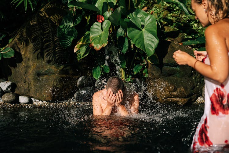 Man Standing In Water Under A Mini Waterfall On A Tropical Vacation 