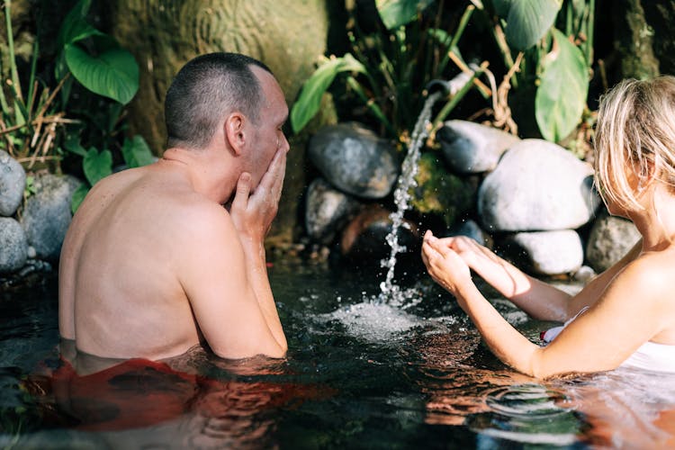 Man And Woman Standing In Water And Catching Flowing Water From A Pipe