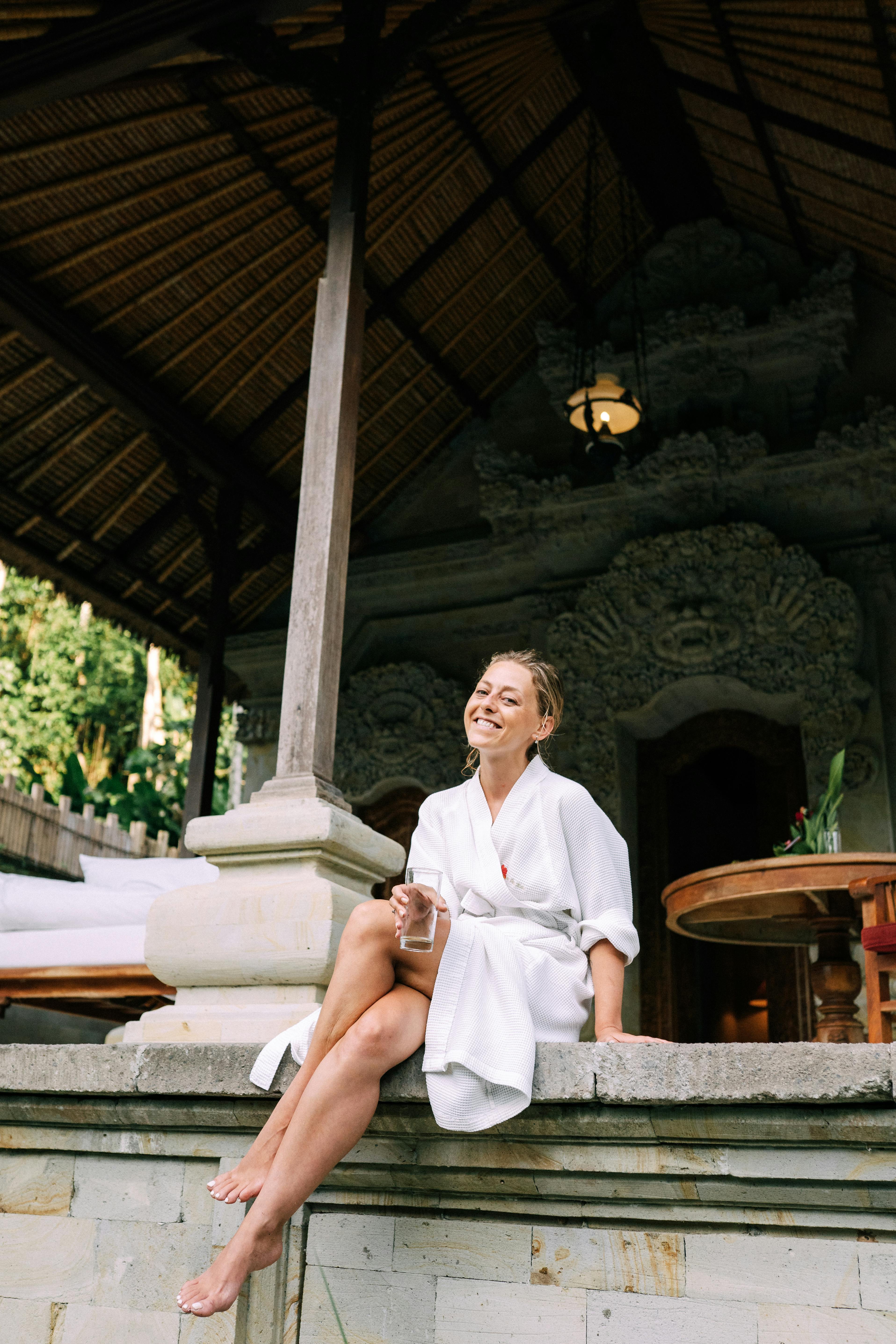 A smiling woman in a robe relaxing at an outdoor luxury resort.