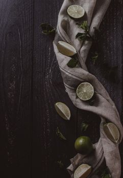 Artistic flatlay showcasing fresh limes and mint leaves on a wooden surface with a textile.