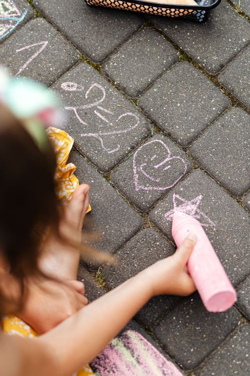 Free A child creatively drawing on pavement using chalk, highlighting artistic expression. Stock Photo