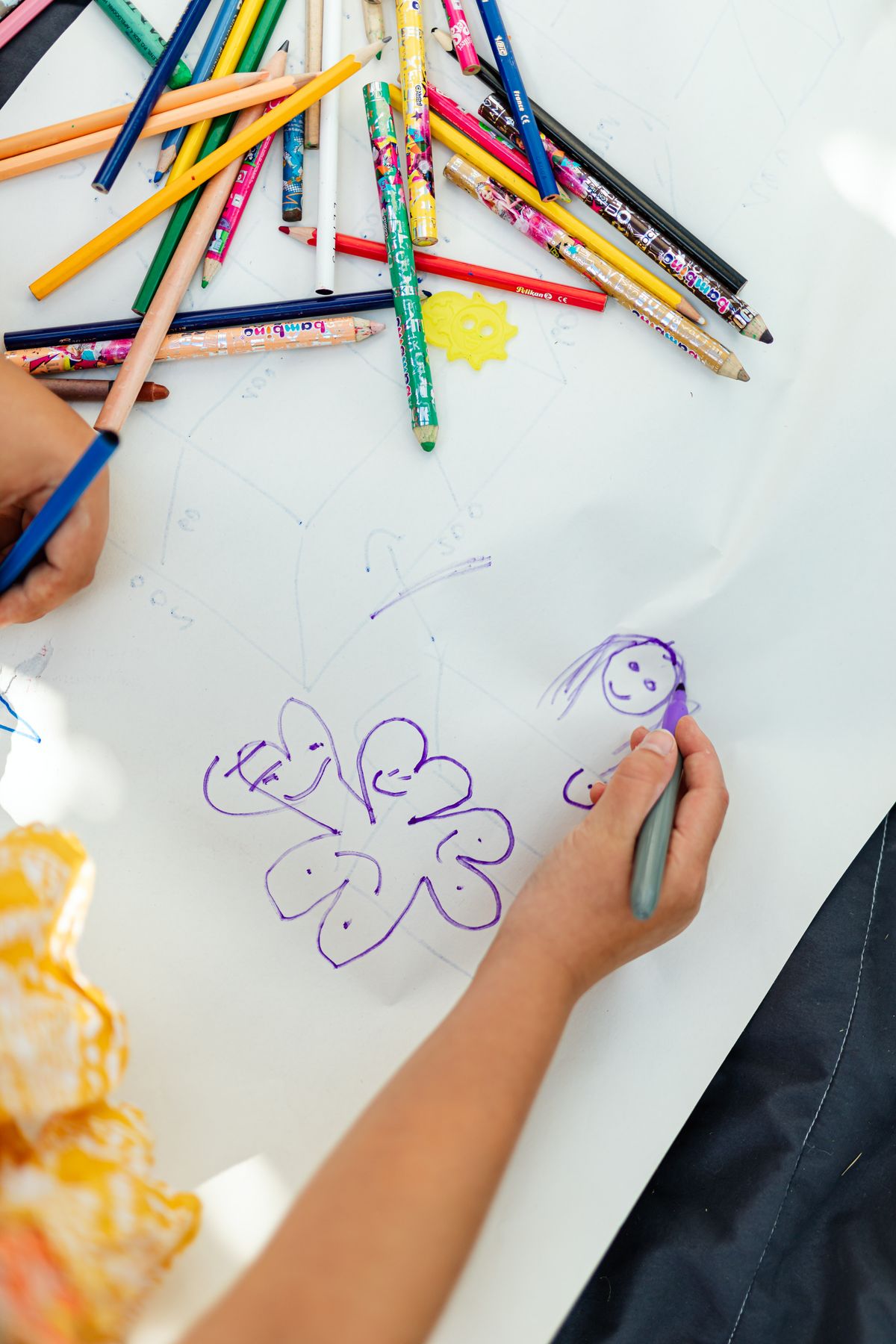 Child drawing a happy puppy on white paper with colored pencils scattered around