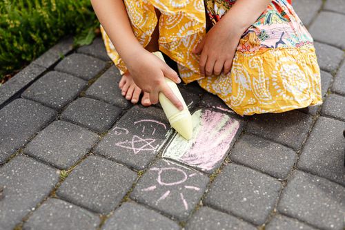 Free A child in a colorful dress draws with chalk on a paved walkway, creating playful doodles. Stock Photo