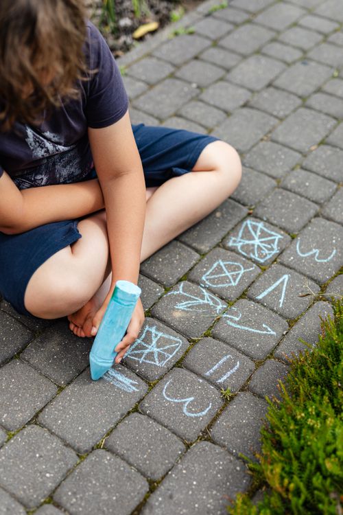 Free A child draws shapes and lines with chalk on a brick pavement outdoors during the day. Stock Photo