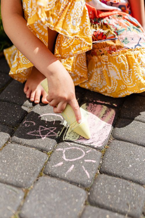 Free A child draws colorful chalk art on pavement during a sunny day. Stock Photo