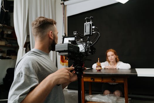Cameraman filming a redhead woman at a studio with dark backdrop.