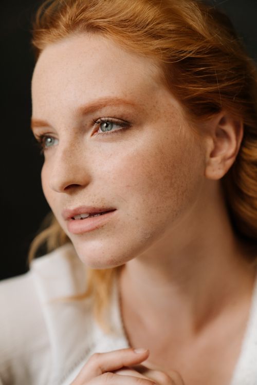 Free Close-up of a redheaded woman with natural beauty and freckles against a dark background. Stock Photo