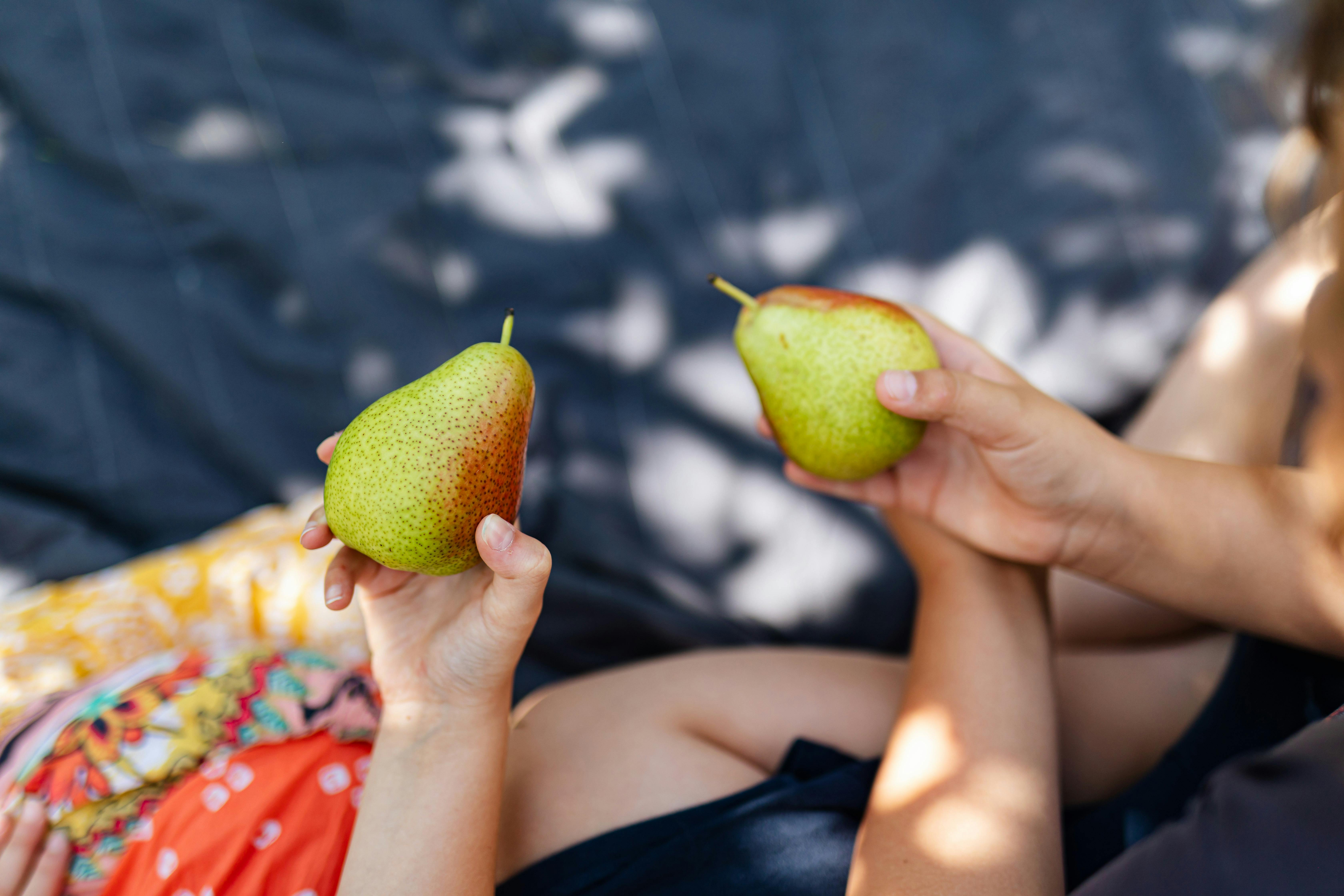 Two children hold ripe pears on a cozy picnic blanket in a sunlit outdoor setting.