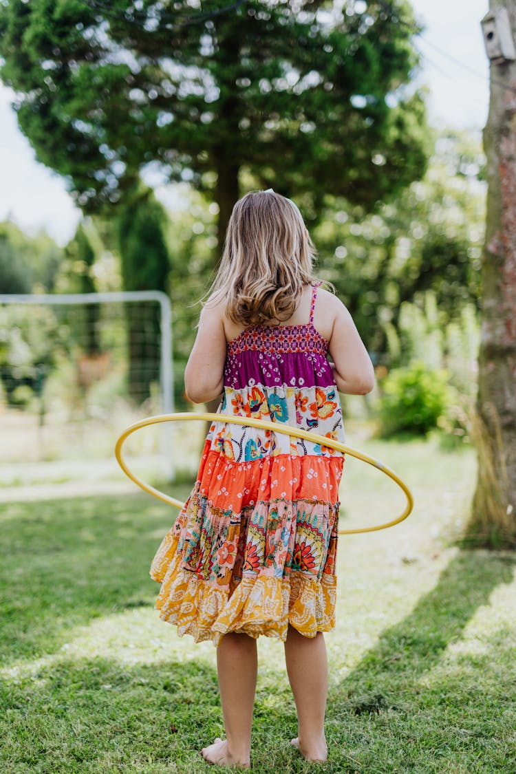 A Girl In Floral Dress Standing On The Green Grass While Doing Hula Hoop