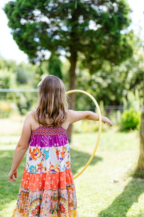 Girl in Pink and White Floral Sleeveless Dress Playing with Yellow Hula Hoop
