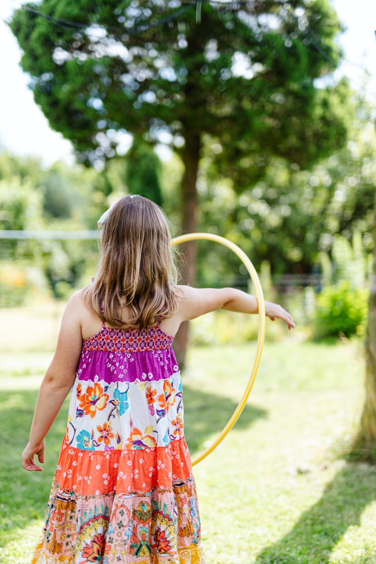 Girl In Pink And White Floral Sleeveless Dress Playing With Yellow Hula Hoop