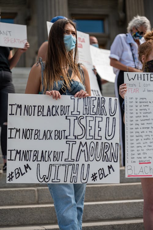 Unrecognizable social justice warriors in masks demonstrating placards with titles about racism on staircase in town