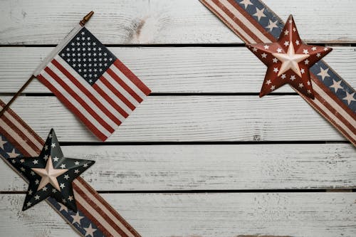 Overhead view of national flag of America between decorative ribbons with stars and stripes on wooden surface