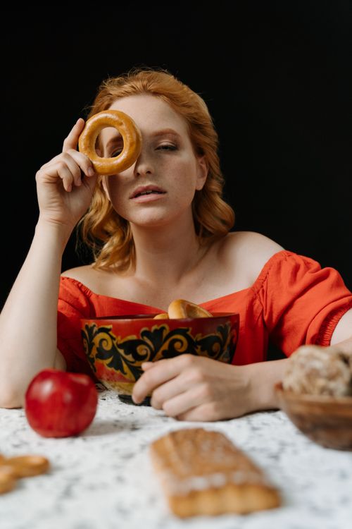 Free A redhead woman in red holds a bagel above her eye, showcasing traditional Russian food. Stock Photo