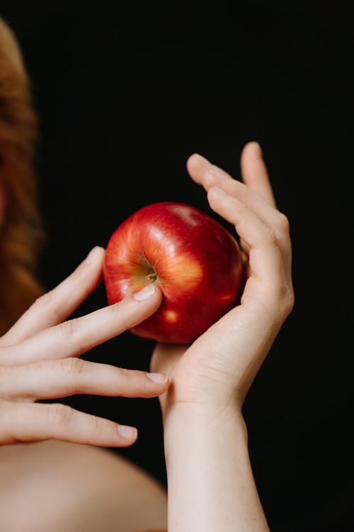 Free Artistic close-up of hands delicately holding a fresh red apple on a dark background. Stock Photo