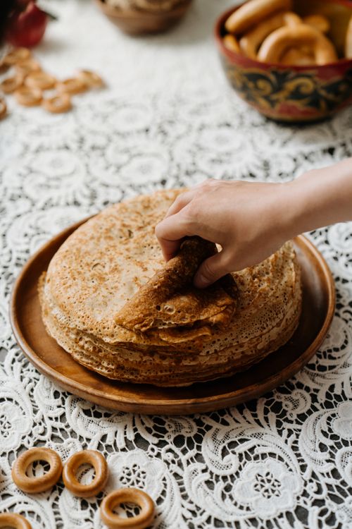 Free A hand picks a blin from a stack on a lace tablecloth, symbolizing Russian culinary tradition. Stock Photo