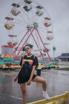 在奥马哈狂欢节上，一位年轻女子在阴天的背景下，于色彩缤纷的摩天轮前摆出姿势