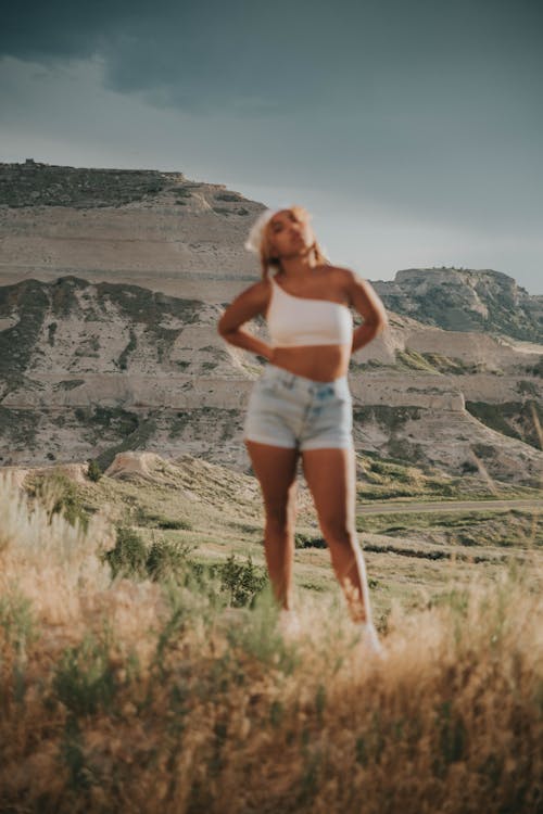 Free Blurred cool ethnic female in casual clothes standing on meadow against rocky mountains in sunny day Stock Photo