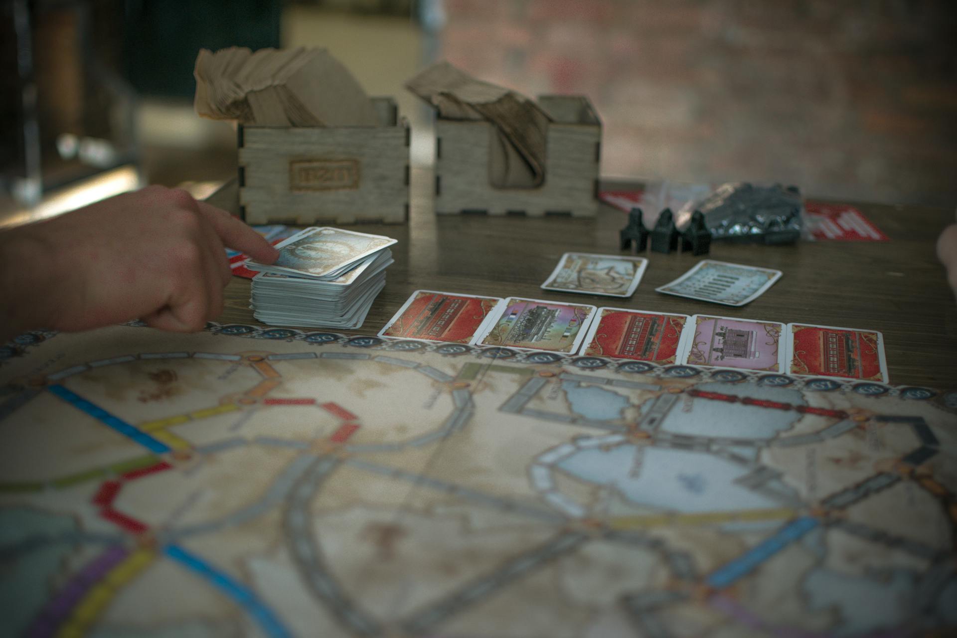 Close-up of a strategic board game session with cards and hands, highlighting game components and play.