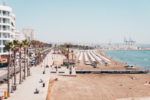 Free Sunny beachfront cityscape with palm trees and beachgoers under a clear sky. Stock Photo