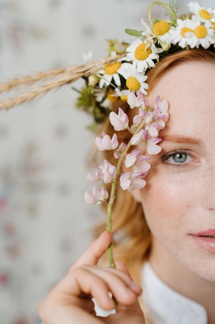 Close-up portrait of a redhead woman wearing a wildflower wreath, highlighting natural beauty.