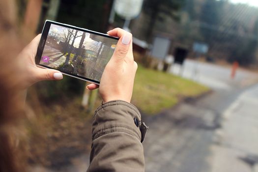 Woman capturing outdoor scenery using a smartphone. Close-up of hands holding the device.